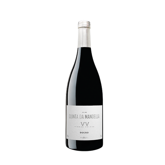 Taça de vinho com garrafa de Manoella Vinhas Velhas da Wine and Soul sobre mesa de madeira.