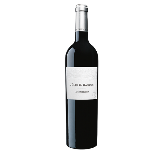 Taça de vinho tinto Julio Bastos Alicante Bouschet da marca Dona Maria com garrafa ao fundo.