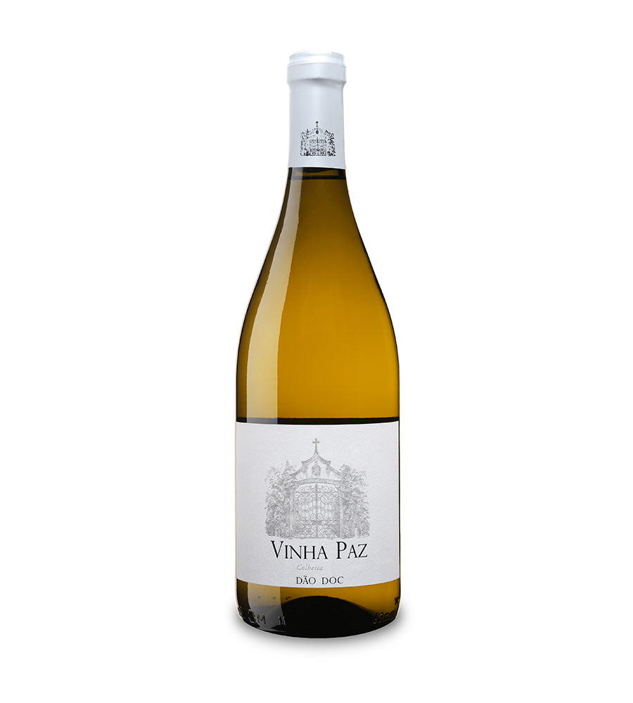 Taça de vinho branco Vinha Paz Branco em uma mesa, destaque para a garrafa de vinho branco ao fundo.