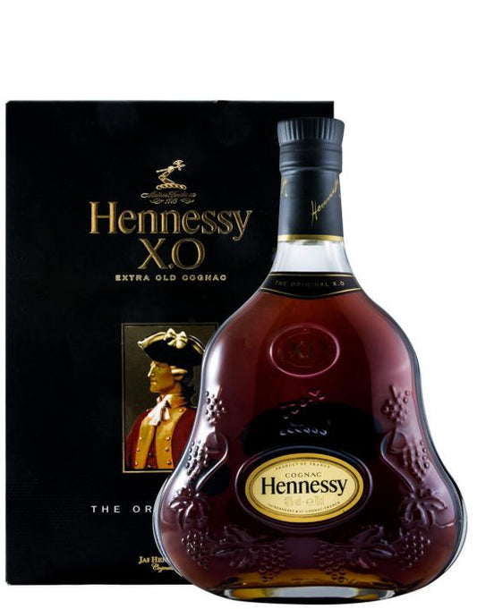 Copo de cristais com destilado de Cognac Hennessy XO, destaque para a cor âmbar escura e a embalagem elegante ao fundo.