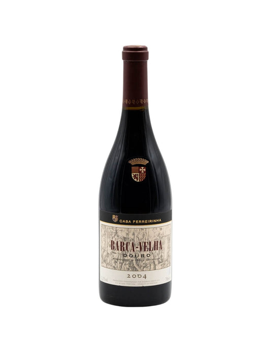 Taça de vinho com garrafa de Barca Velha 2004, destaque para rótulo clássico e cor rubi intensa.
