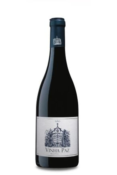 Taça de vinho tinto Vinha Paz Reserva Tinto 2016, com garrafa de vinho tinto ao fundo.